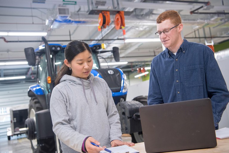 Penn State student and professor in front of agricultural machinery.